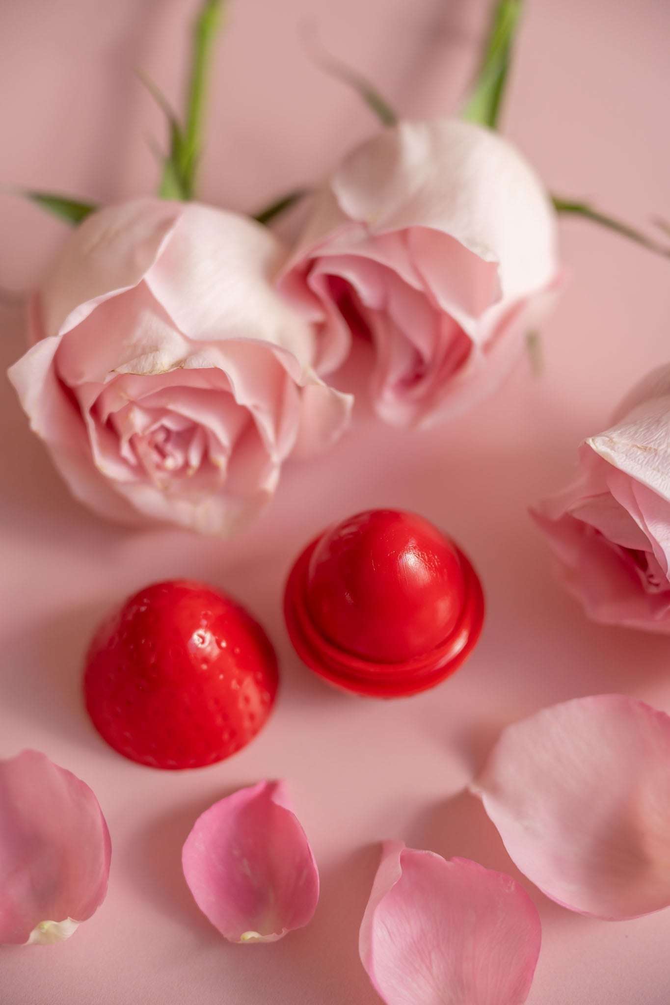 Red lip butter balm dome and open cap with pink rose blossoms nearby