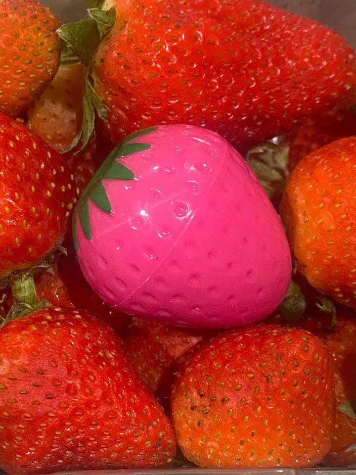 Pink strawberry-shaped lip butter in open cap, surrounded by strawberries.