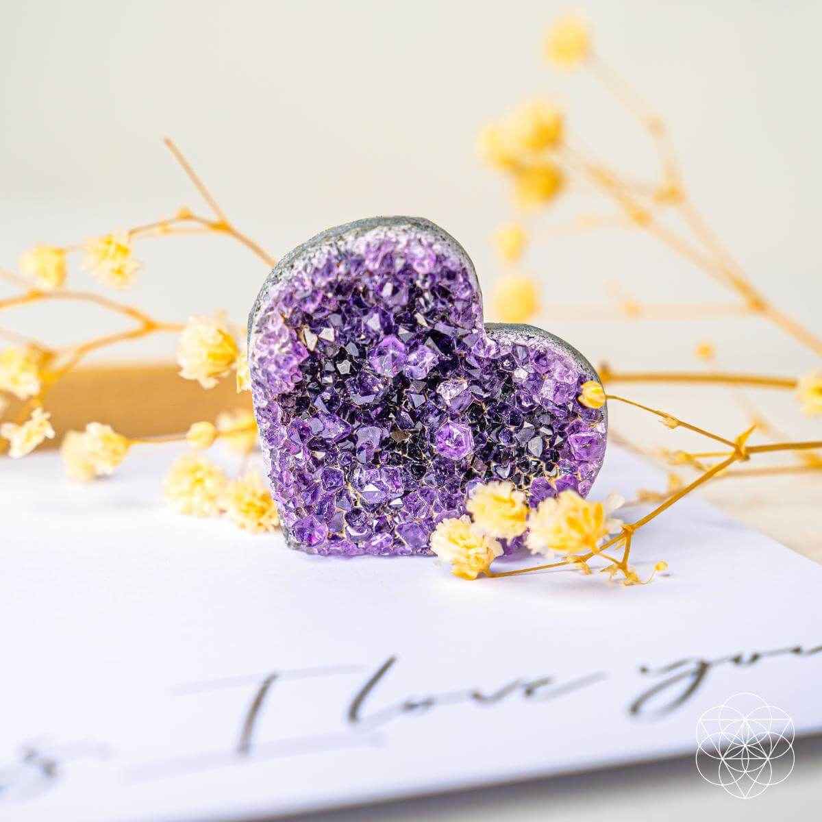 Purple amethyst heart cluster with faceted crystal texture, stone on a rounded base.