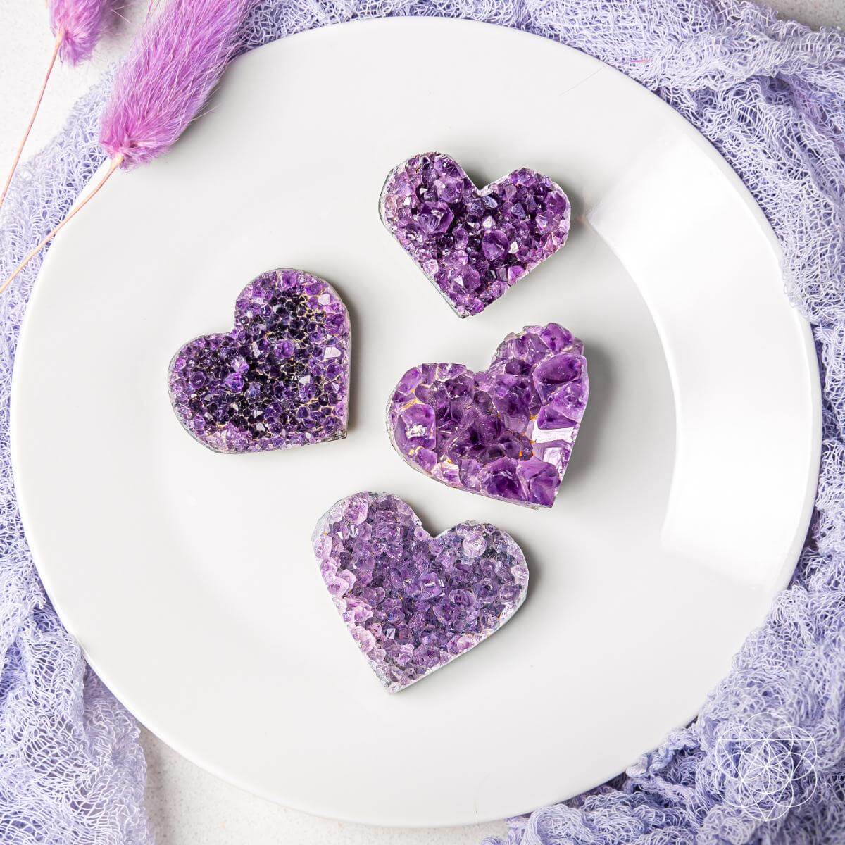 Purple amethyst heart clusters arranged on a white plate, five heart stones shown.
