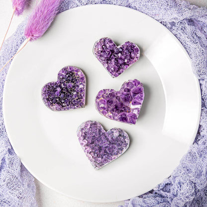 Purple amethyst heart clusters arranged on a white plate, five heart stones shown.