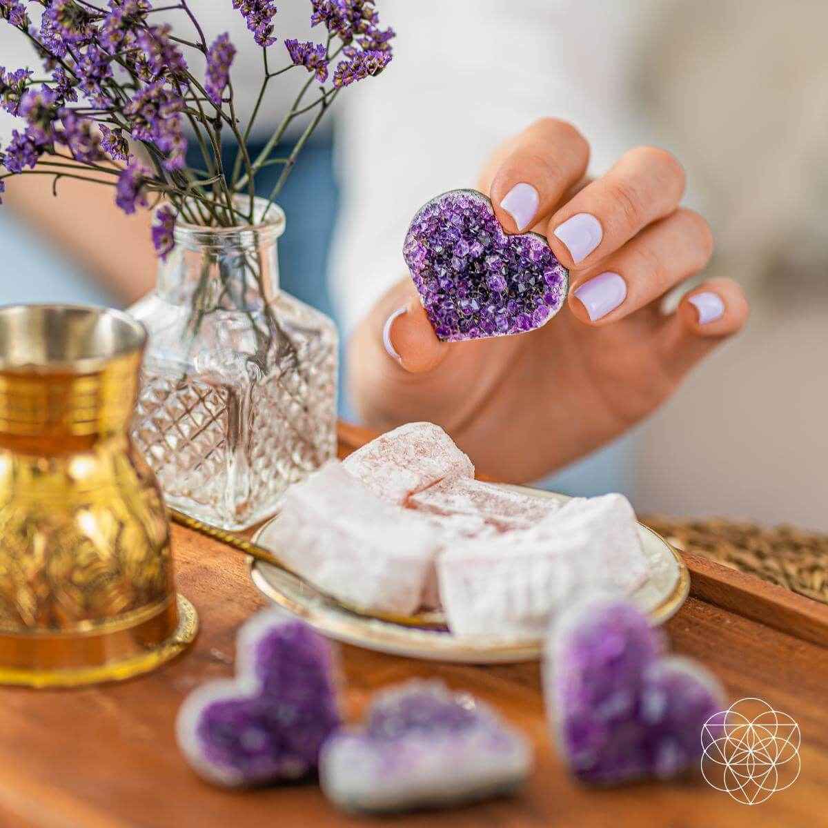 Purple amethyst heart cluster held in a hand, glittering druzy crystal surface.