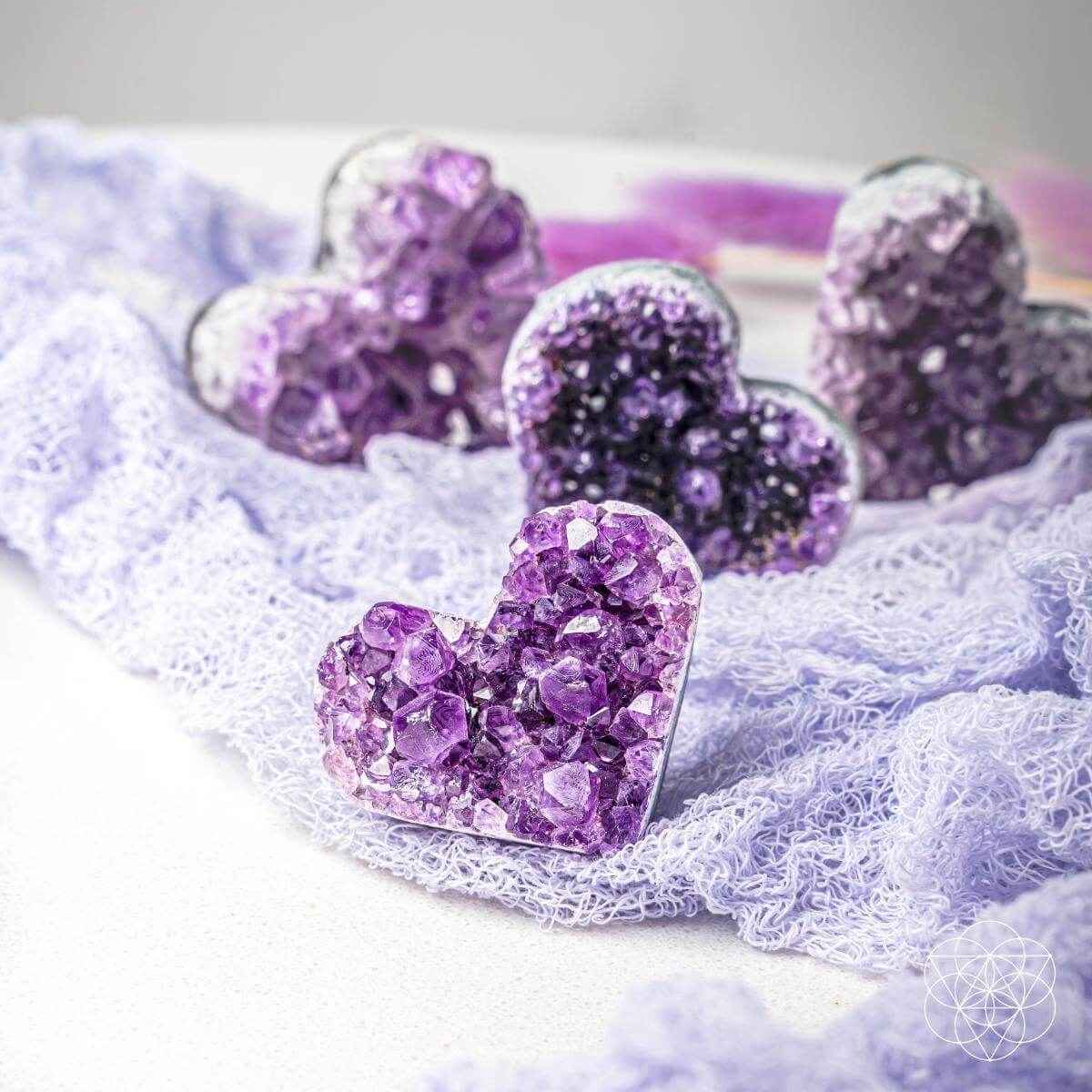 Purple amethyst heart cluster stones nestled in white fuzzy fiber, multiple hearts visible.