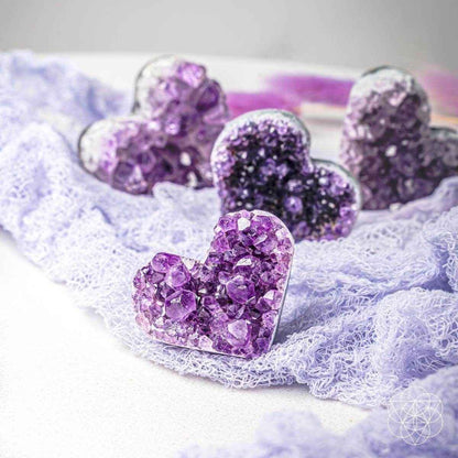 Purple amethyst heart cluster stones nestled in white fuzzy fiber, multiple hearts visible.