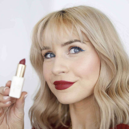 Red matte lipstick held in hand with gold case visible