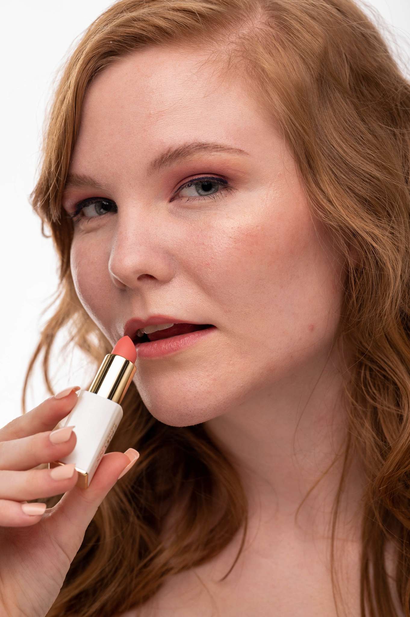 Woman applying matte lipstick, showing maroon shade on lips and gold cap