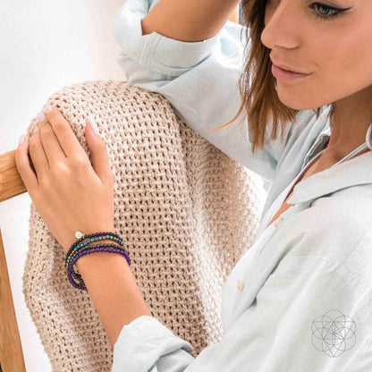 Purple and black beaded wrap bracelet set with round silver charm on a wrist