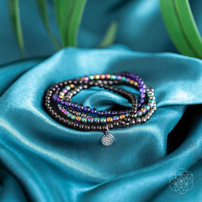 Purple and black beaded wrap bracelet set with a round silver charm on teal satin fabric