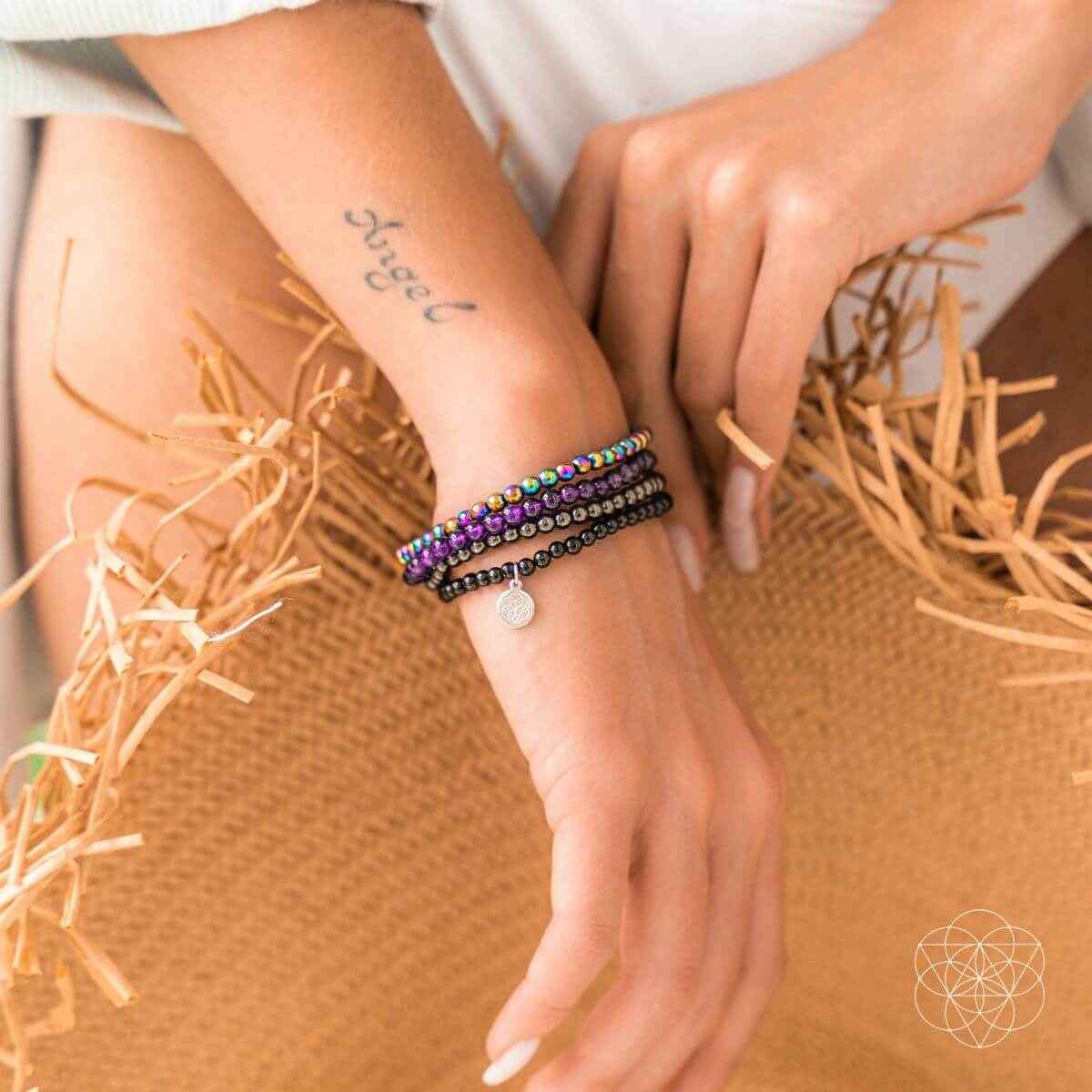 Stacked beaded wrap bracelets on wrist with purple, black beads, and a small silver charm