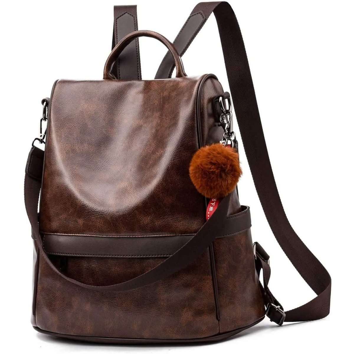 Brown backpack purse with front flap, top handles, adjustable shoulder strap, and pom-pom charm