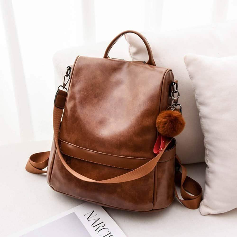 Brown backpack purse with front flap, top handle, crossbody strap, and pom-pom charm