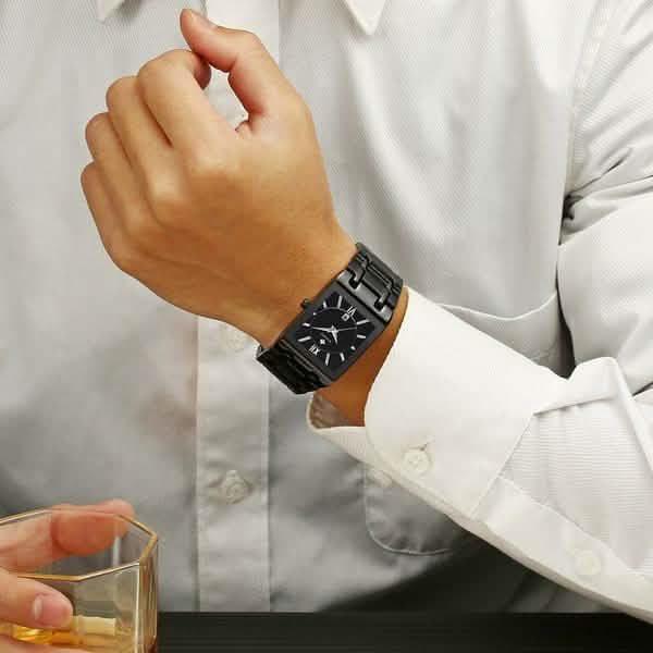 Men’s square date watch on wrist with black dial and black metal link bracelet
